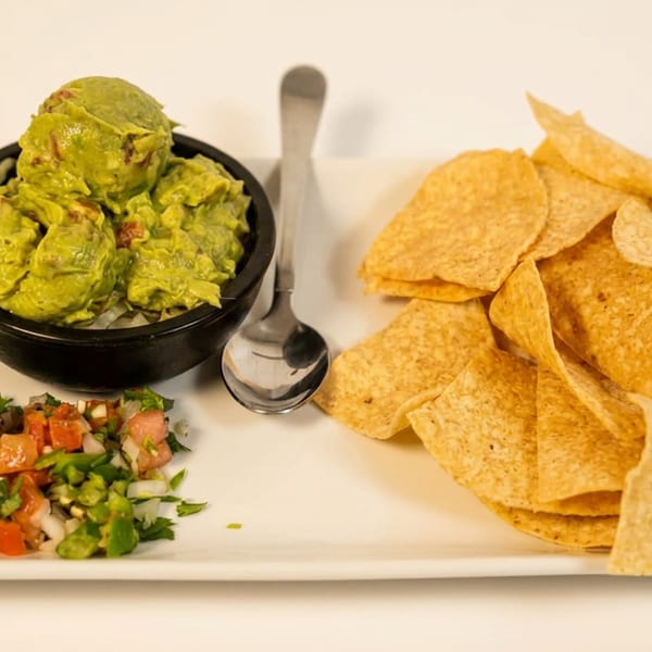 Plate of guacamole, tortilla chips, and fresh pico de gallo with a spoon.