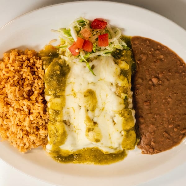 Plate of Mexican food featuring green enchiladas topped with melted cheese, rice, refried beans, and shredded lettuce with tomatoes.