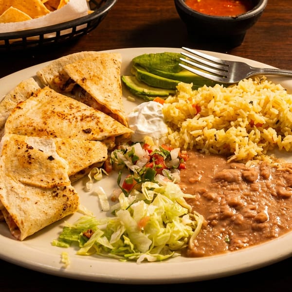 Mexican combination plate with grilled quesadillas, rice, refried beans, lettuce salad, avocado, sour cream, and salsa with tortilla chips.